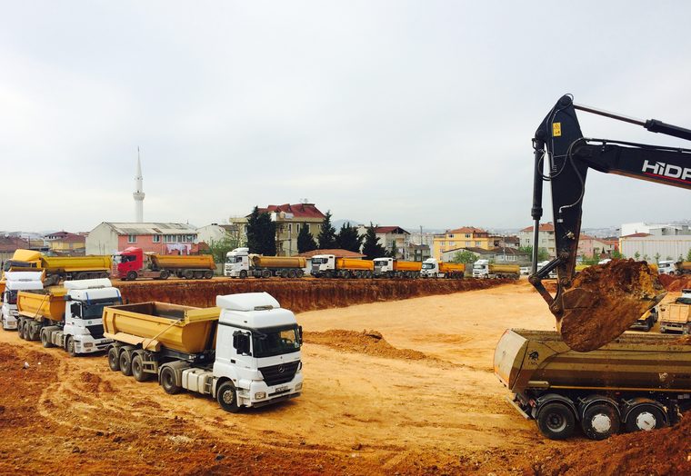 Temel hafriyat sahasında sıralanmış damperli kamyonlar ve ekskavatör